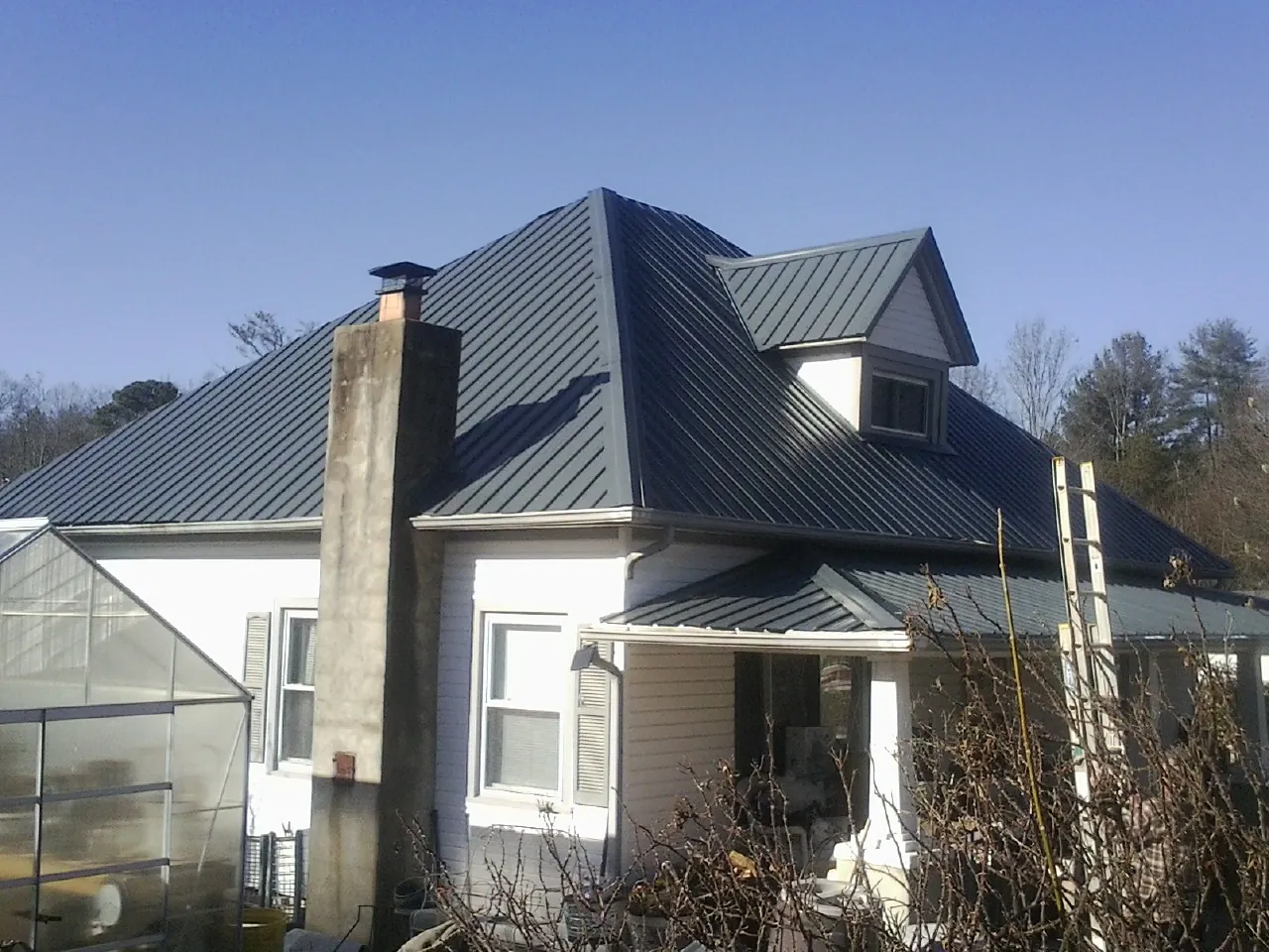 Dark blue standing seam metal roof on a white farmhouse with dormer — Slate & Tile Roof Repair by Roofing Brothers in Candor