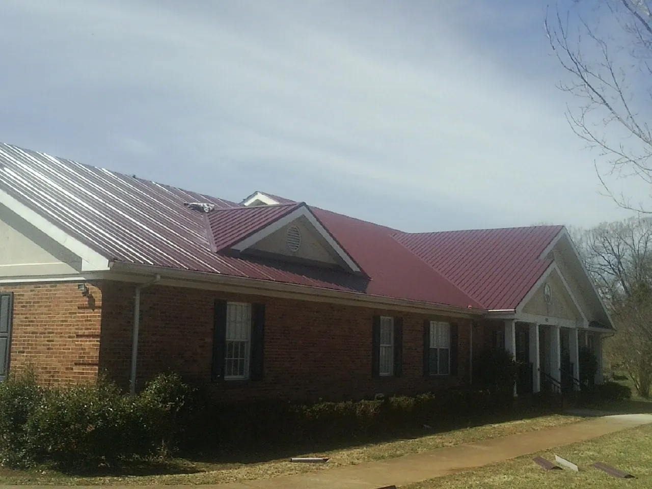 Red metal roof with gabled entries on a long brick building, from a Hail Damage Roof Repair job in Candor