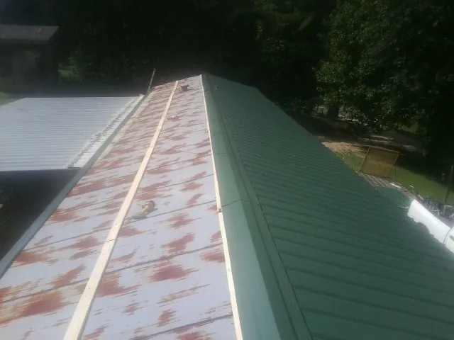 Old rusted panels beside newly installed green metal roofing — Wind Damage Roof Repair by Roofing Brothers in Candor