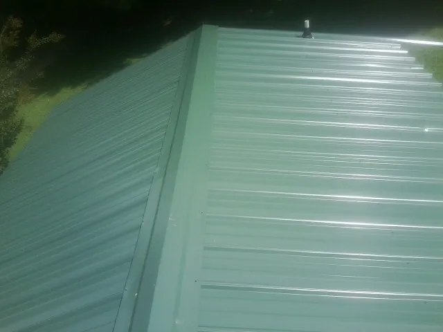 New green metal panels meeting at the ridge of a roof — Flat Roof Repair work by our crew in Candor