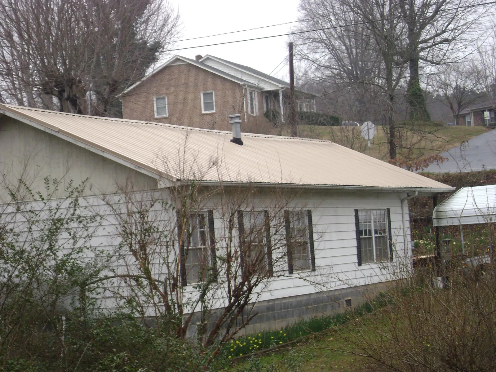 Tan metal roof on a white sided house set into a hillside — Commercial Roofing by Roofing Brothers in Candor